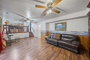 Living area featuring ceiling fan, a textured ceiling, wood finished floors, wainscoting, and wooden walls