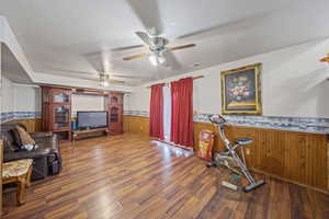 Living room featuring a wainscoted wall, wooden walls, wood finished floors, a ceiling fan, and a textured ceiling