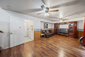 Living room with wood finished floors, a textured ceiling, a ceiling fan, and a wainscoted wall