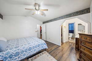 Bedroom with dark wood finished floors, vaulted ceiling, baseboards, ceiling fan, and ensuite bath