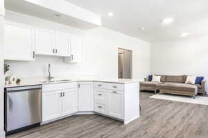 Kitchen with dishwasher, light wood-style flooring, a peninsula, light countertops, and white cabinets