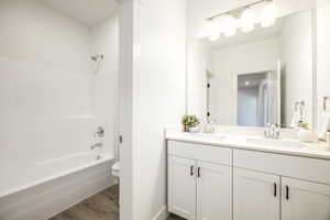 Full bath featuring toilet, wood finished floors, double vanity, shower / tub combination, and baseboards