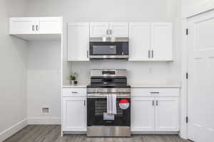 Kitchen with stainless steel appliances, white cabinetry, and light wood-type flooring