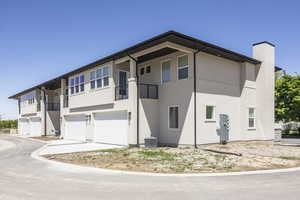 View of front facade with a garage, stucco siding, a balcony, and a chimney