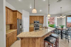 Kitchen with appliances with stainless steel finishes, a sink, light tile patterned floors, brown cabinets, and decorative backsplash