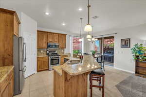 Kitchen featuring stainless steel appliances, a sink, brown cabinetry, light tile patterned floors, and a kitchen breakfast bar