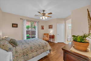 Bedroom featuring wood finished floors, access to exterior, baseboards, ceiling fan, and ensuite bathroom