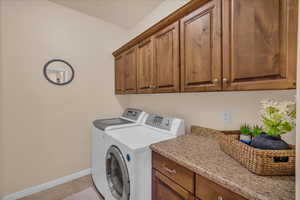 Laundry room with cabinet space, washer and dryer, baseboards, and light tile patterned floors