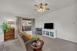 Carpeted living area featuring vaulted ceiling, a ceiling fan, and baseboards