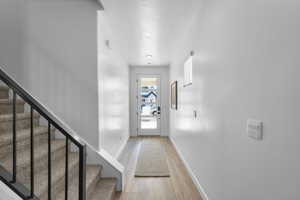 Doorway with light wood-style floors, stairs, baseboards, and a textured ceiling