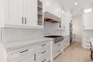 Kitchen featuring stainless steel appliances, white cabinets, light stone countertops, recessed lighting, and decorative backsplash