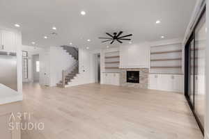 Unfurnished living room featuring stairs, a ceiling fan, recessed lighting, light wood-type flooring, and a glass covered fireplace