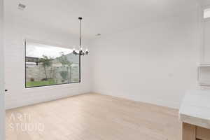Unfurnished dining area with a chandelier, light wood finished floors, and baseboards