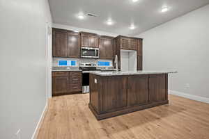 Kitchen with stainless steel appliances, a sink, baseboards, dark brown cabinetry, and light wood-style floors