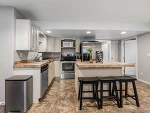 Kitchen with stainless steel appliances, a breakfast bar area, a sink, a kitchen island, and light countertops
