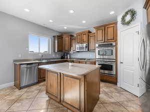 Kitchen with appliances with stainless steel finishes, a sink, a kitchen island, recessed lighting, and light tile patterned flooring