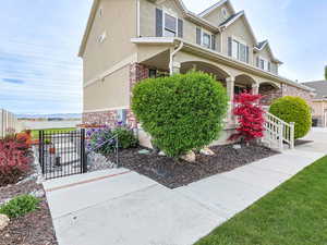 View of property exterior with covered porch, fence, a gate, stucco siding, and brick siding