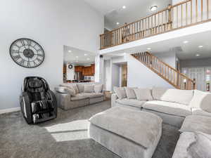 Carpeted living area with stairs, recessed lighting, baseboards, and a towering ceiling