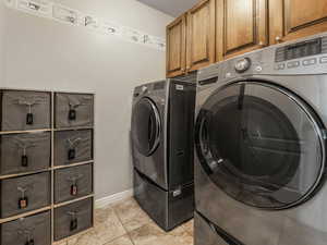 Laundry room featuring washer and clothes dryer, cabinet space, baseboards, and light tile patterned floors