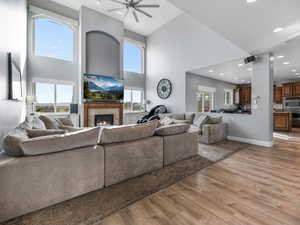 Living room with a towering ceiling, light wood-type flooring, ceiling fan, a lit fireplace, and recessed lighting