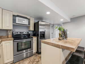 Kitchen with stainless steel appliances, cream cabinets, light countertops, a kitchen breakfast bar, and a kitchen island