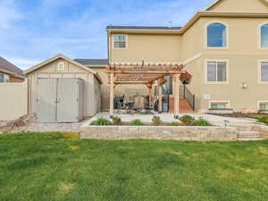 Rear view of house with a storage unit, stucco siding, a patio, an outdoor structure, and a pergola