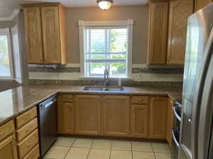 Kitchen featuring appliances with stainless steel finishes, a sink, tasteful backsplash, light tile patterned flooring, and ornamental molding