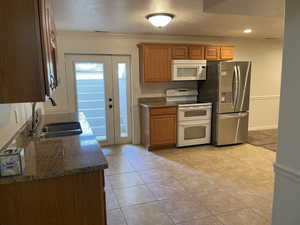 Kitchen with white appliances, a sink, crown molding, a textured ceiling, and dark stone countertops