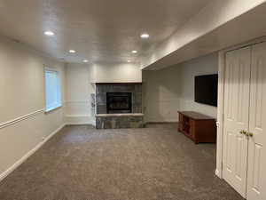 Unfurnished living room featuring carpet flooring, a stone fireplace, recessed lighting, baseboards, and a textured ceiling