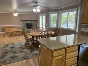 Kitchen with stainless steel dishwasher, a ceiling fan, wood finished floors, crown molding, and a stone fireplace