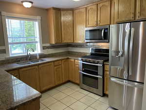 Kitchen featuring stainless steel appliances, a sink, light tile patterned flooring, backsplash, and dark stone countertops
