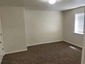 Spare room with dark colored carpet, a textured ceiling, and baseboards