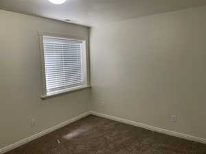 Unfurnished room featuring dark carpet and baseboards
