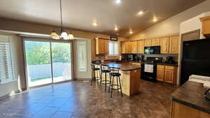 Kitchen with black appliances, dark countertops, a breakfast bar area, healthy amount of natural light, and vaulted ceiling