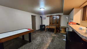 Recreation room featuring a wood stove, dark carpet, and a textured ceiling