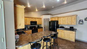 Kitchen featuring black appliances, dark countertops, vaulted ceiling, light brown cabinetry, and a peninsula