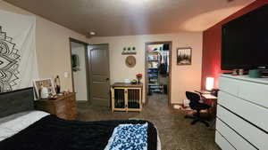 Carpeted bedroom featuring a spacious closet, a textured ceiling, a desk, and a closet