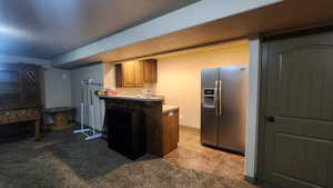 Kitchen featuring stainless steel fridge, a peninsula, light countertops, brown cabinetry, and light colored carpet