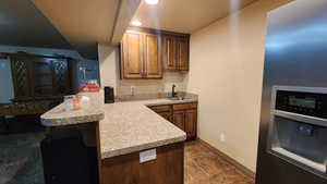 Kitchen with a sink, light countertops, a peninsula, baseboards, and dark tile patterned floors