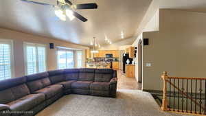 Living area featuring ceiling fan, vaulted ceiling, light colored carpet, and a chandelier