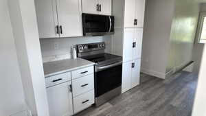 Kitchen with stainless steel electric range oven, wood finished floors, light stone counters, white cabinetry, and baseboards