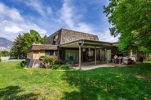 Rear view of house featuring a patio, mansard roof, a lawn, brick siding, and a mountain view