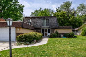 View of property with mansard roof, brick siding, a front lawn, an attached garage, and concrete driveway