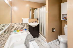 Master Bathroom featuring toilet, vanity, a tub with jets, a stall shower, and marble finish flooring