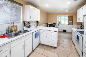 Kitchen featuring white appliances, a peninsula, a sink, white cabinetry, and tile counters