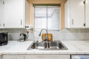 Kitchen featuring a sink, white cabinets, and light countertops