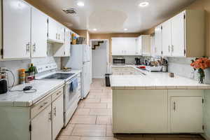 Kitchen with white appliances, backsplash, recessed lighting, tile counters, and a peninsula