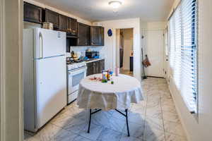 Second Kitchen with white appliances, light marble finish flooring, dark brown cabinets, under cabinet range hood, and light countertops