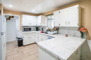 Kitchen with stainless steel microwave, backsplash, a sink, freestanding refrigerator, and white cabinets
