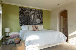 Bedroom featuring arched walkways, crown molding, carpet, and baseboards